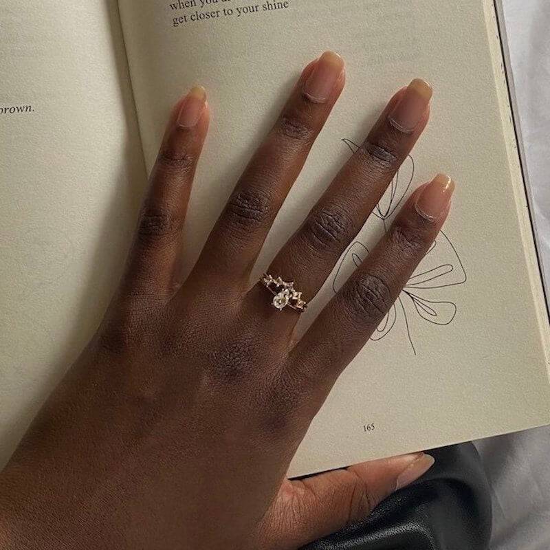 Close-up of a hand with a delicate ring resting on an open book with a minimalist line drawing on the page