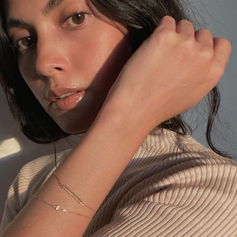 Close-up of a woman with brown eyes wearing a beige ribbed top and delicate gold bracelets in warm natural light