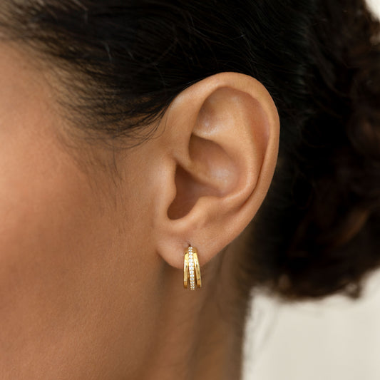 Close-up of an ear wearing Gemstone Huggie Hoop Earrings - Livna with triple gold vermeil bands and cubic zirconia stones