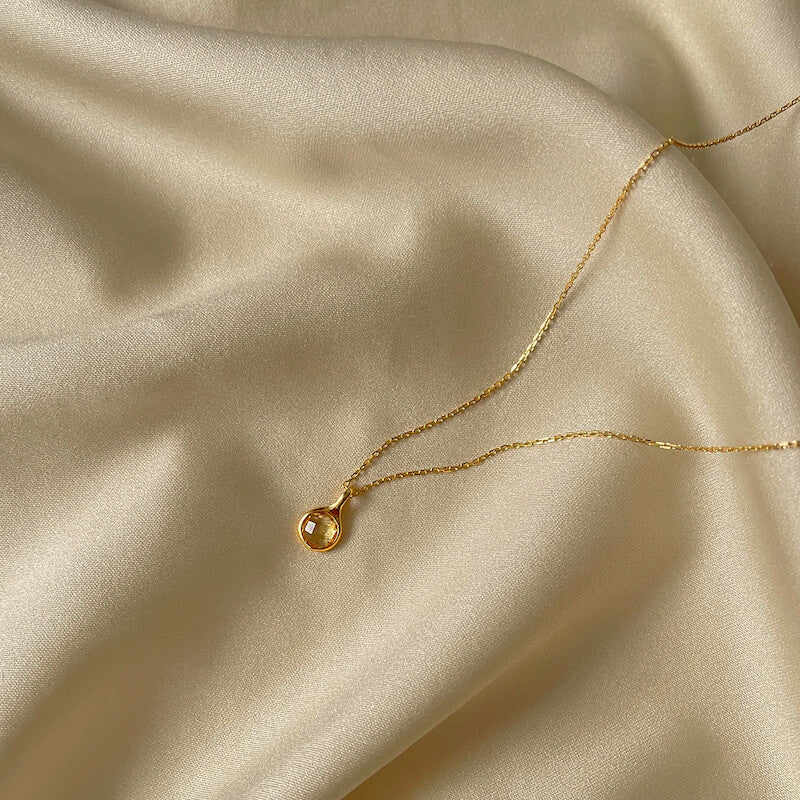 Delicate gold necklace with a small circular pendant resting on smooth beige satin fabric
