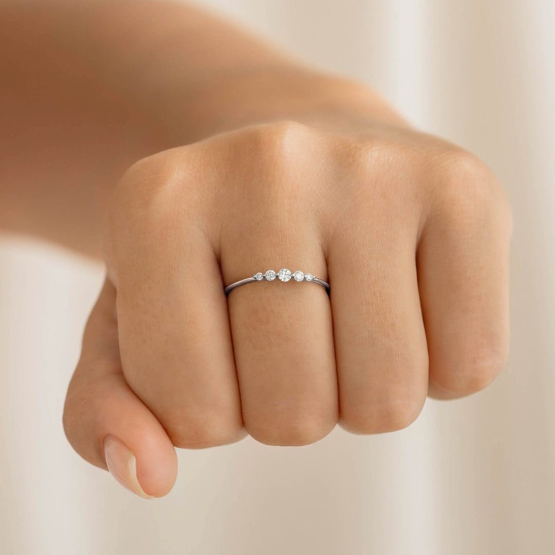 Close-up of a hand wearing the Graduated Diamond Ring White Gold - Dahlia featuring five sparkling diamonds on a white gold band