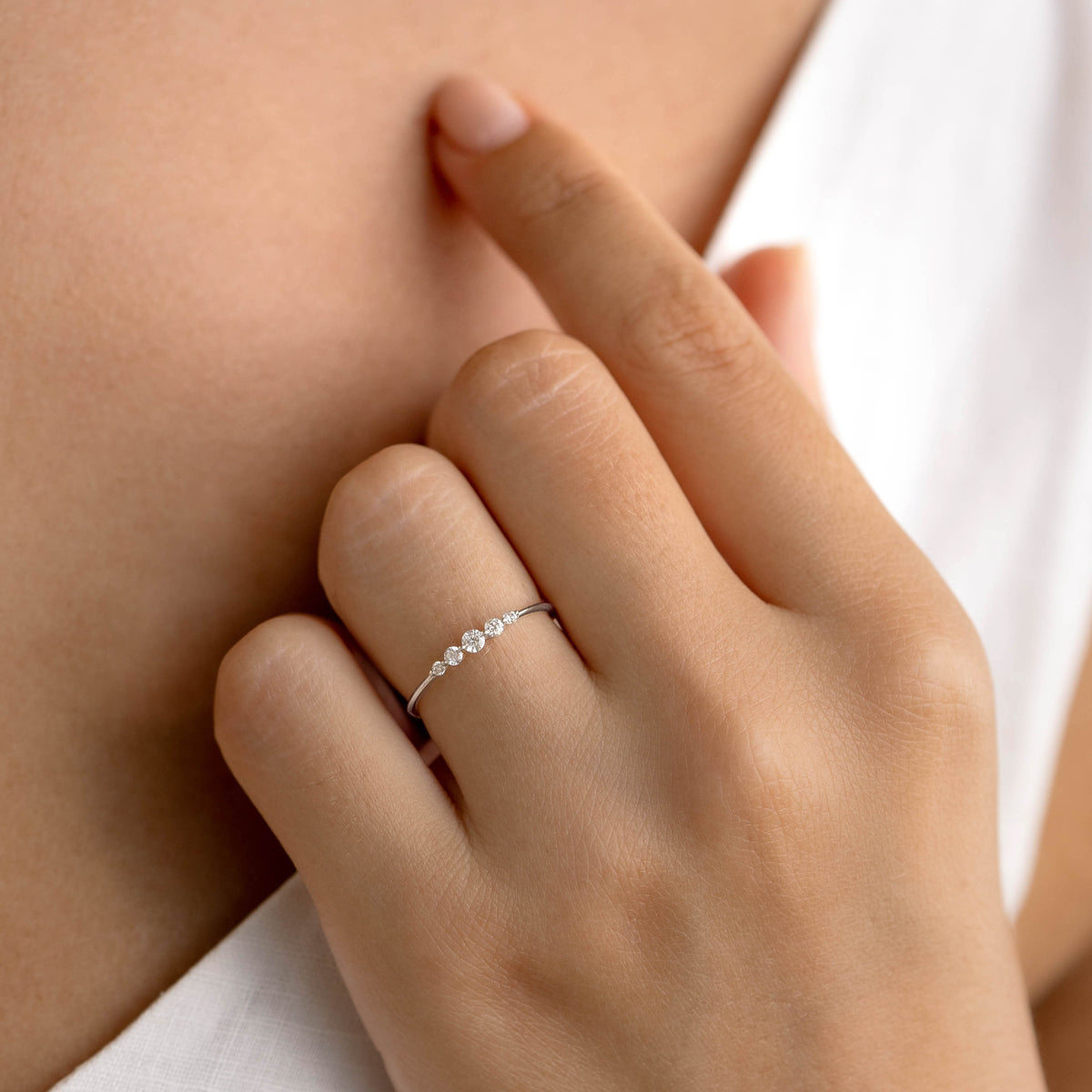 Close-up of a hand wearing the Graduated Diamond Ring White Gold - Dahlia with five varying diamonds on a white gold band