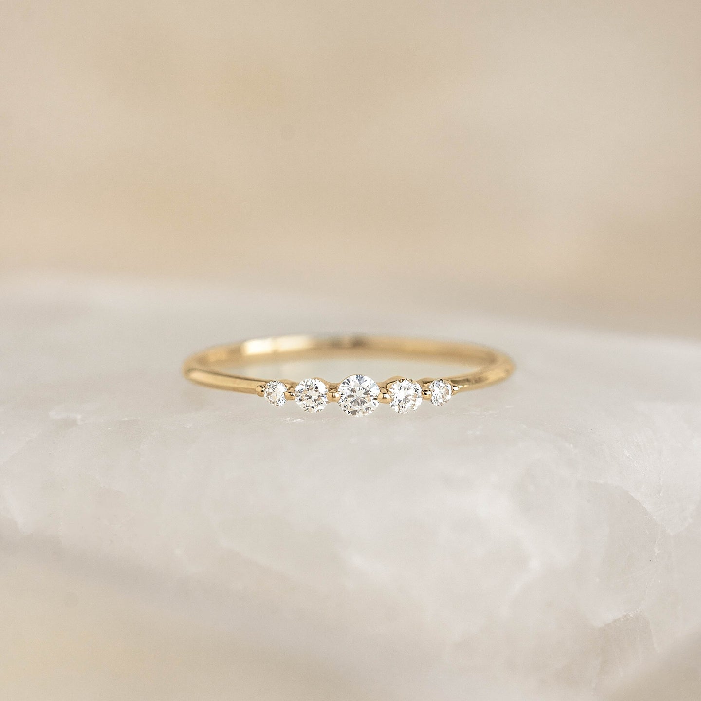 Close-up of Graduated Diamond Ring 14k Gold - Dahlia with five diamonds on a slim yellow gold band on a soft background