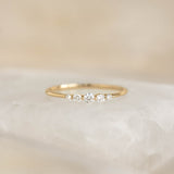 Close-up of Graduated Diamond Ring 14k Gold - Dahlia with five diamonds on a slim yellow gold band on a soft background