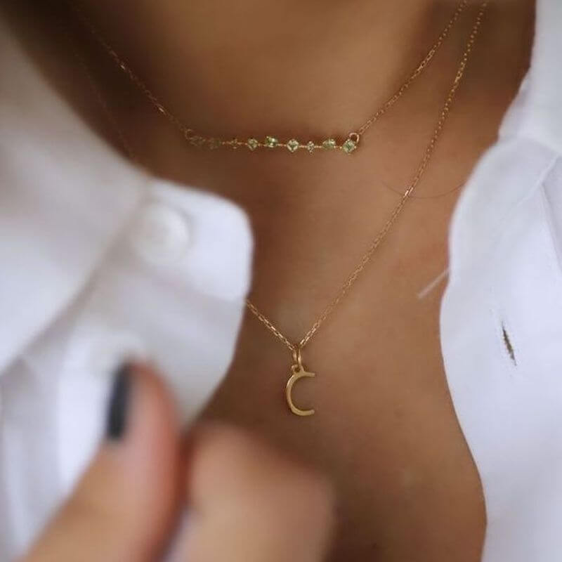 Close-up of a woman wearing layered delicate gold necklaces with a crescent pendant and small stones on a light skin tone