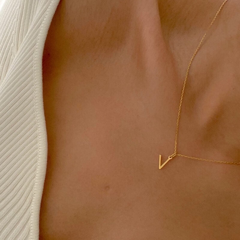 Close-up of a person wearing a delicate gold chain necklace with a small V-shaped pendant and a white ribbed top