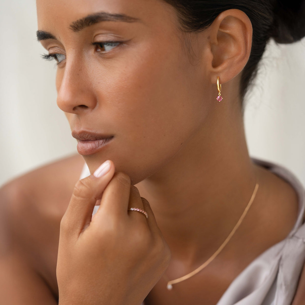 Close-up of woman wearing July Birthstone Drop Huggie Earrings - Pink Tourmaline with gold vermeil setting and soft natural light