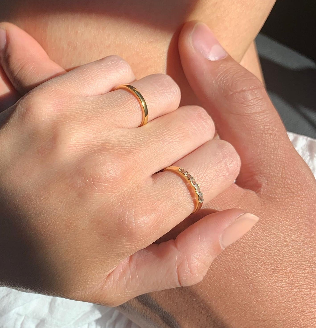 Close-up of two hands with matching gold rings holding each other in soft natural light