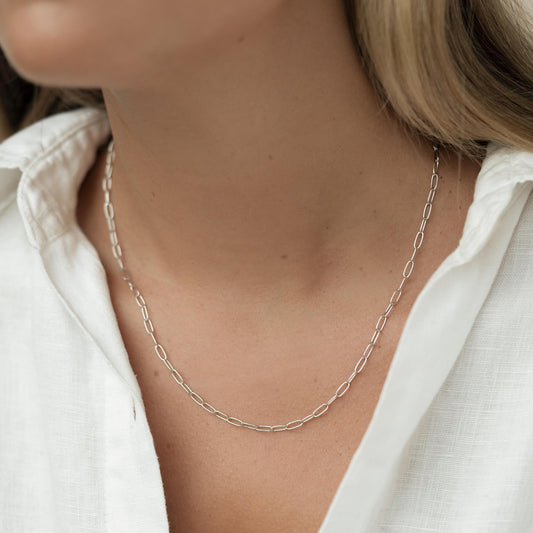 Close-up of a woman wearing a Paperclip Necklace Silver with a white linen shirt on a neutral background