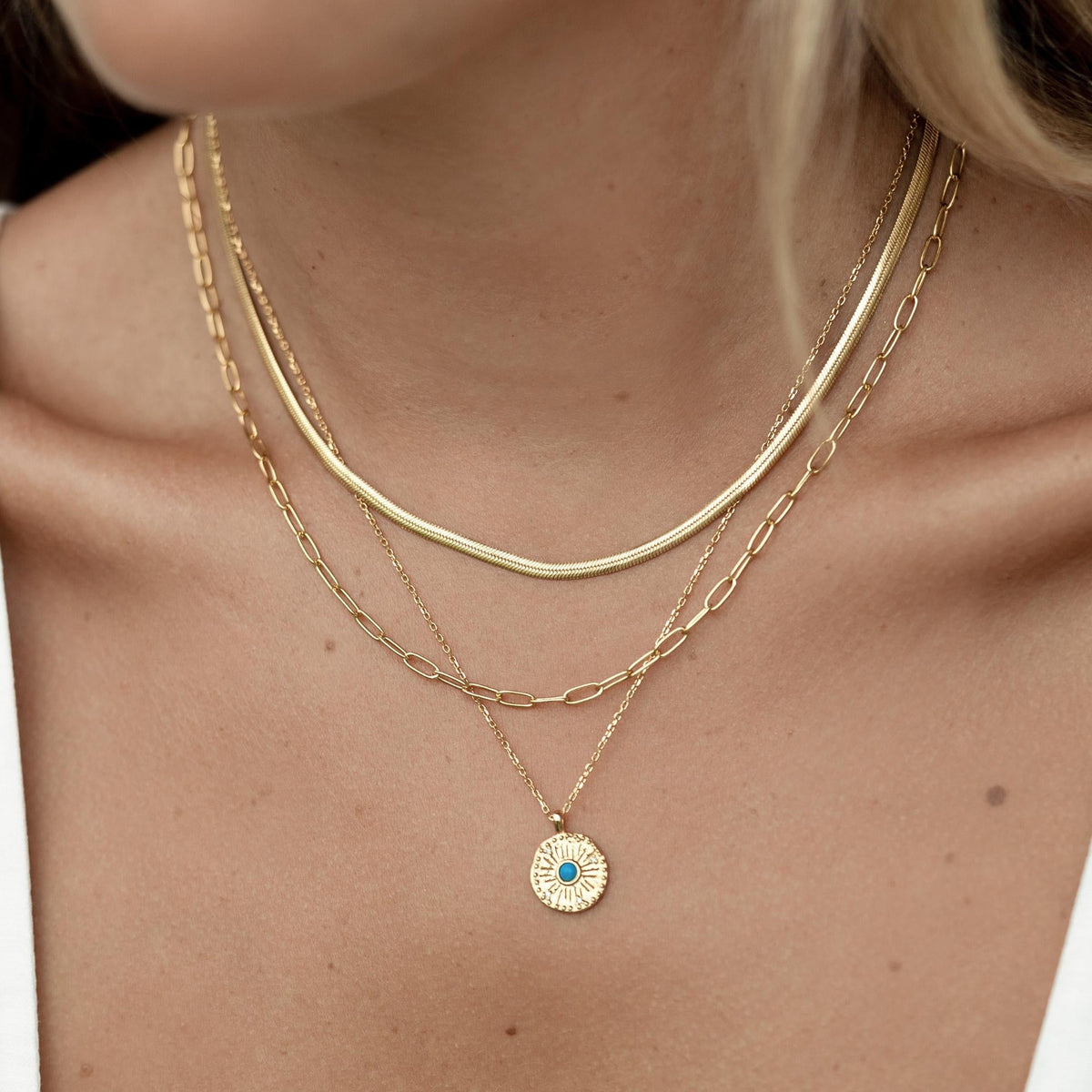 Close-up of a woman wearing the Gold Coin Necklace - Odina with layered gold chain necklaces on a neutral background