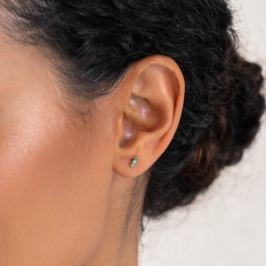 Close-up of a woman wearing Trio Emerald Stud Earrings 14k Gold - Yara featuring three small emeralds on one ear