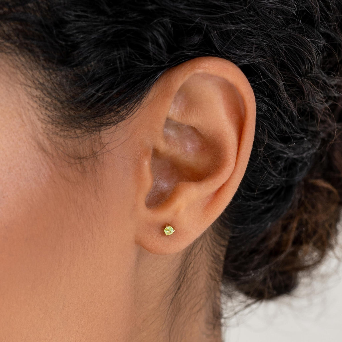 Close-up of a woman wearing August Birthstone Stud Earrings 14k Gold - Olivine with a natural skin tone background
