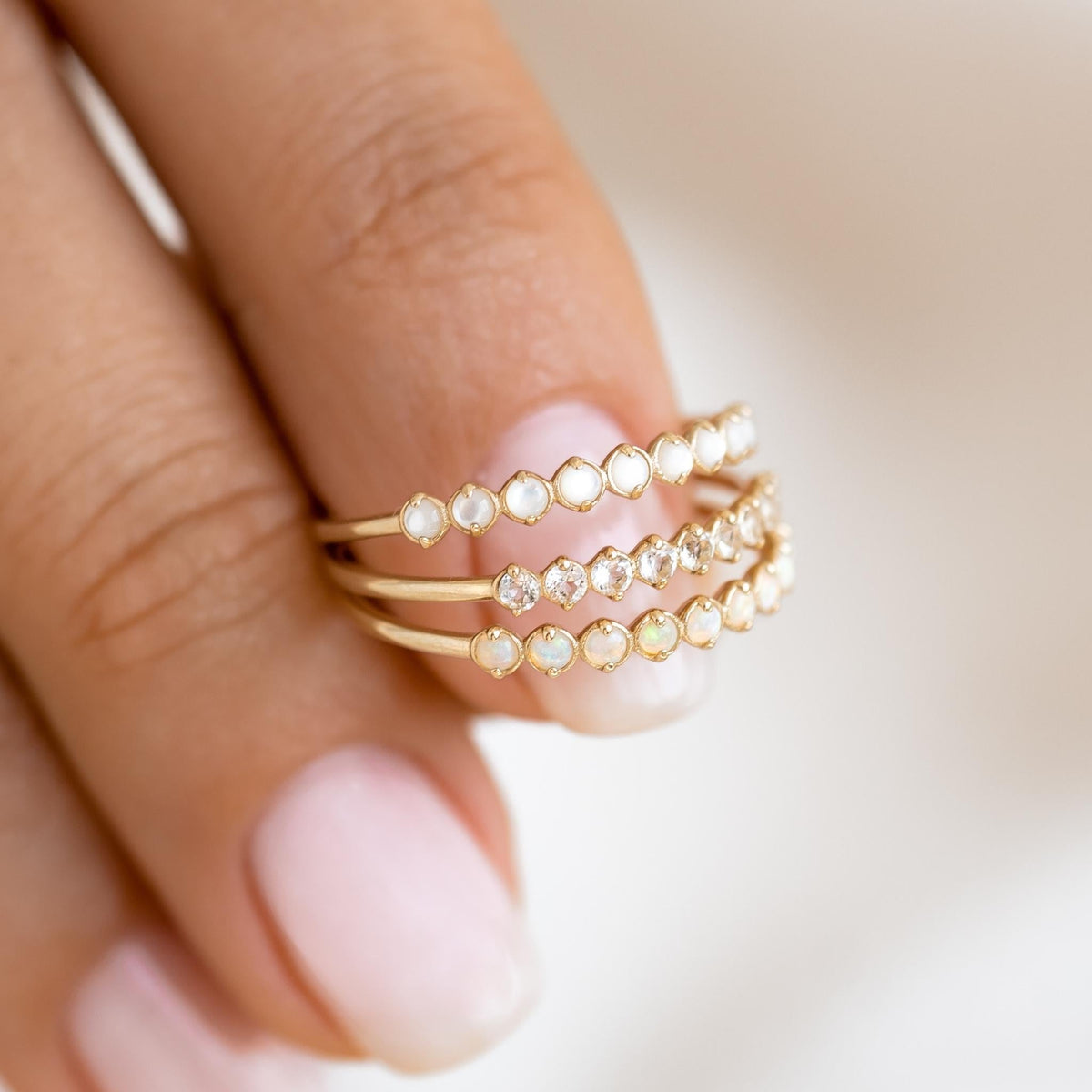 October Birthstone Ring 14k Gold - Opal featuring three delicate gold bands with shimmering opal stones on a hand close-up