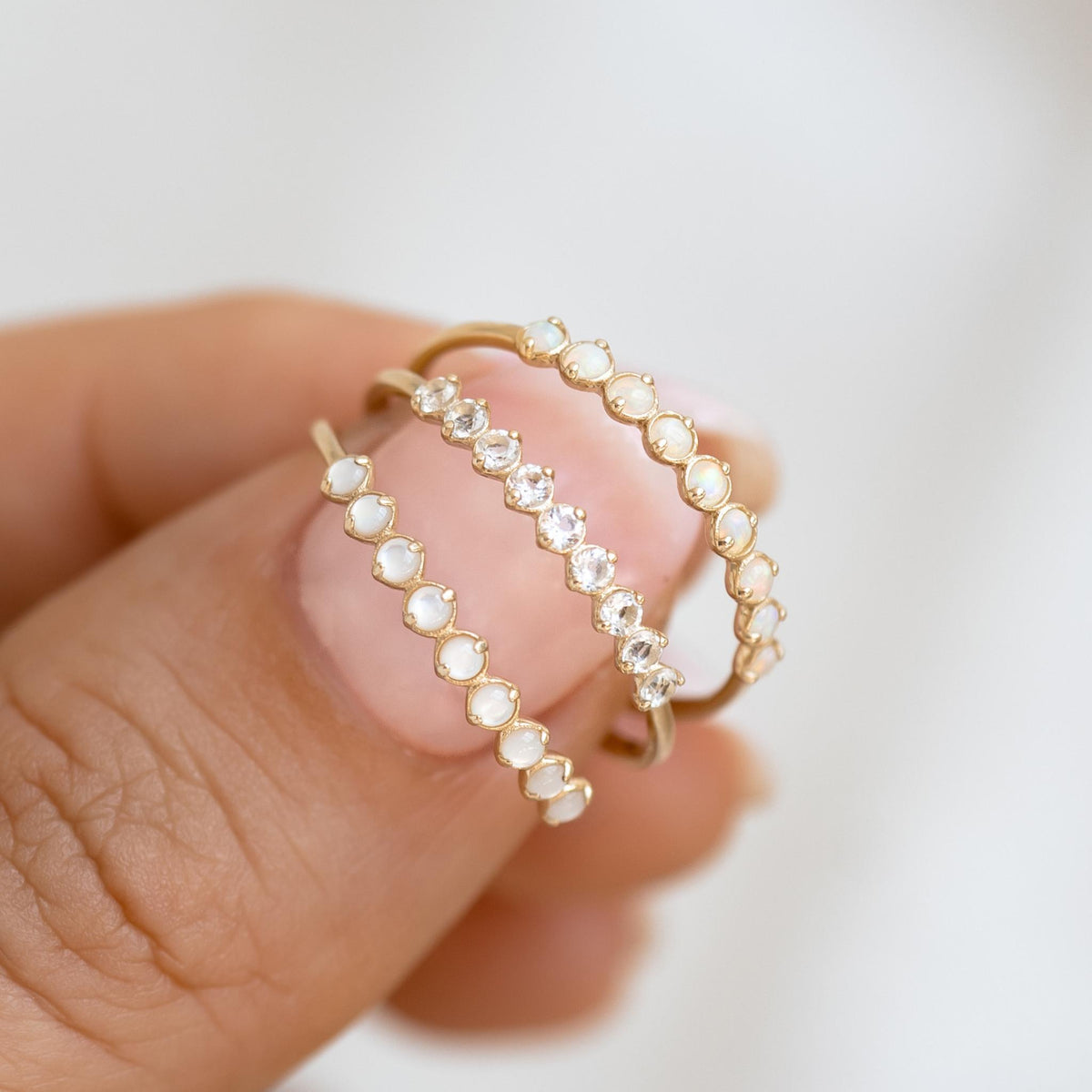 Close-up of three April Birthstone Ring 14k Gold - White Topaz rings held between fingers on a neutral background