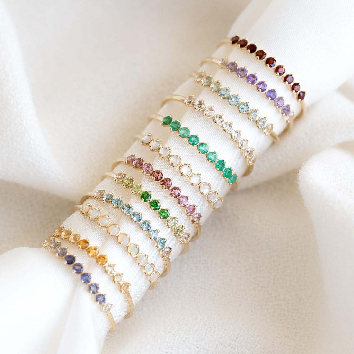 May Birthstone Ring 14k Gold - Green Chalcedony and assorted birthstone rings displayed on white fabric background