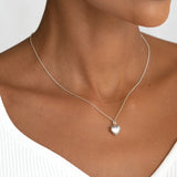 Close-up of a woman wearing a Puffy Heart Necklace Silver with a puffy heart pendant on a delicate silver chain