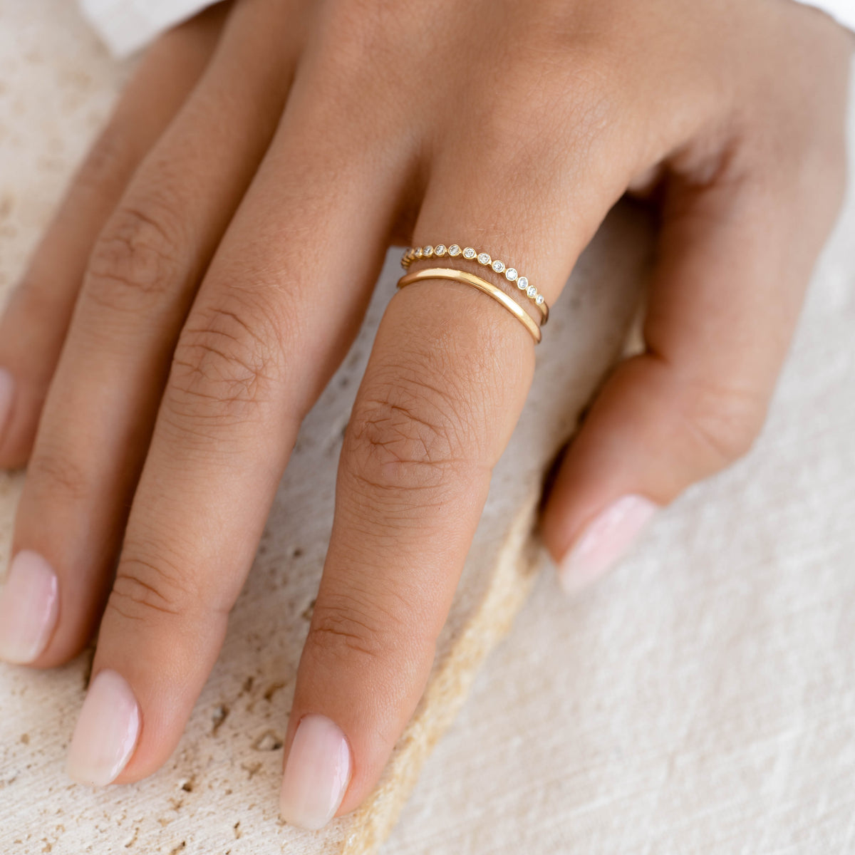 Close-up of a hand wearing Diamond Wavy Ring 14k Gold - Amara with bezel-set diamonds on a natural background