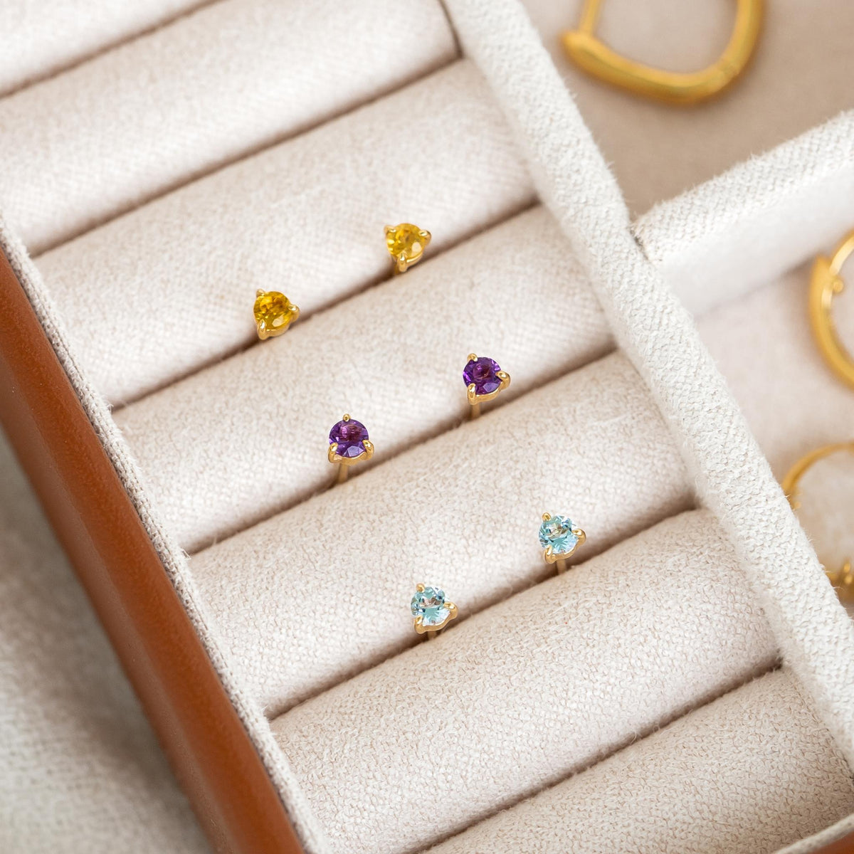 March Birthstone Stud Earrings 14k Gold - Blue Topaz pair with other gemstone studs displayed in a jewelry case