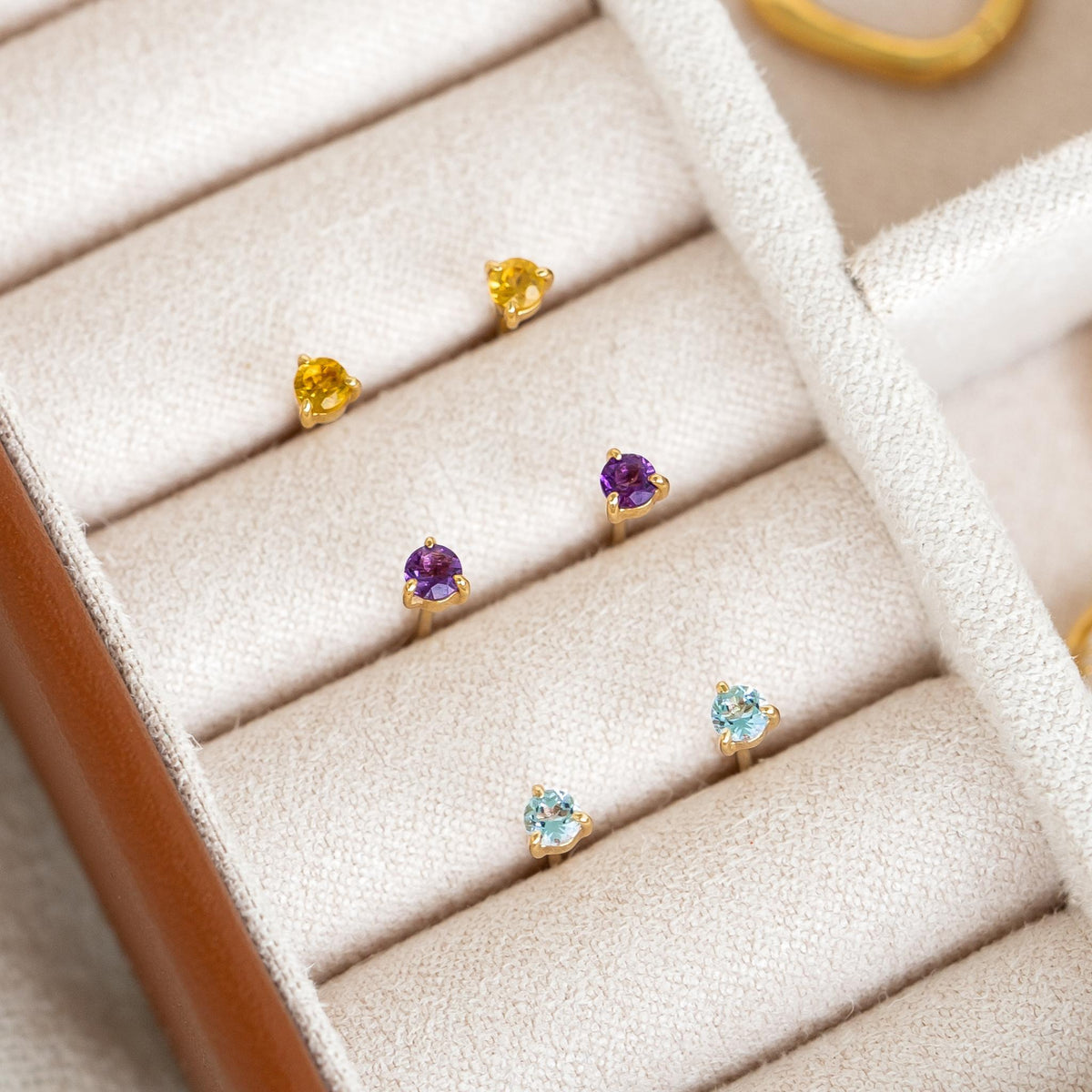 February Birthstone Stud Earrings 14k Gold - Amethyst displayed in a beige jewelry organizer with yellow and blue pairs nearby