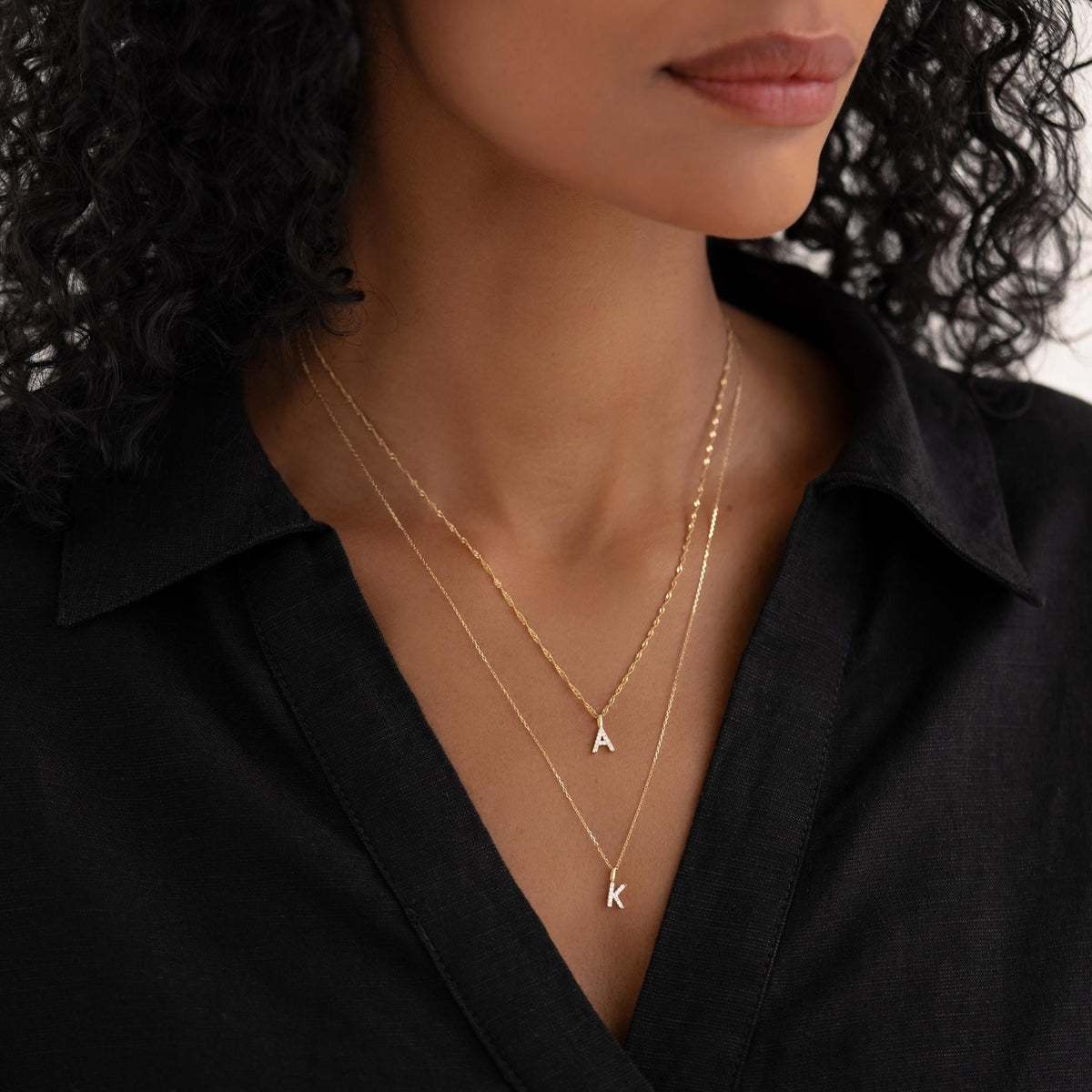 Close-up of a woman wearing layered Diamond Initial Pendant 14k Gold - G necklaces with a black shirt