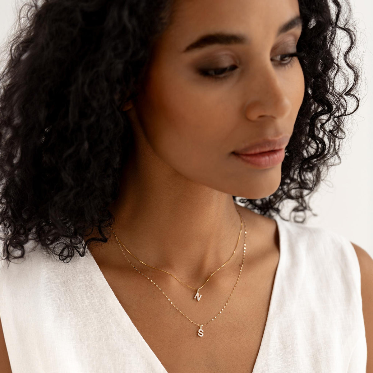 Close-up of woman wearing layered 14k gold necklaces with Diamond Initial Pendant 14k Gold - I on a white top