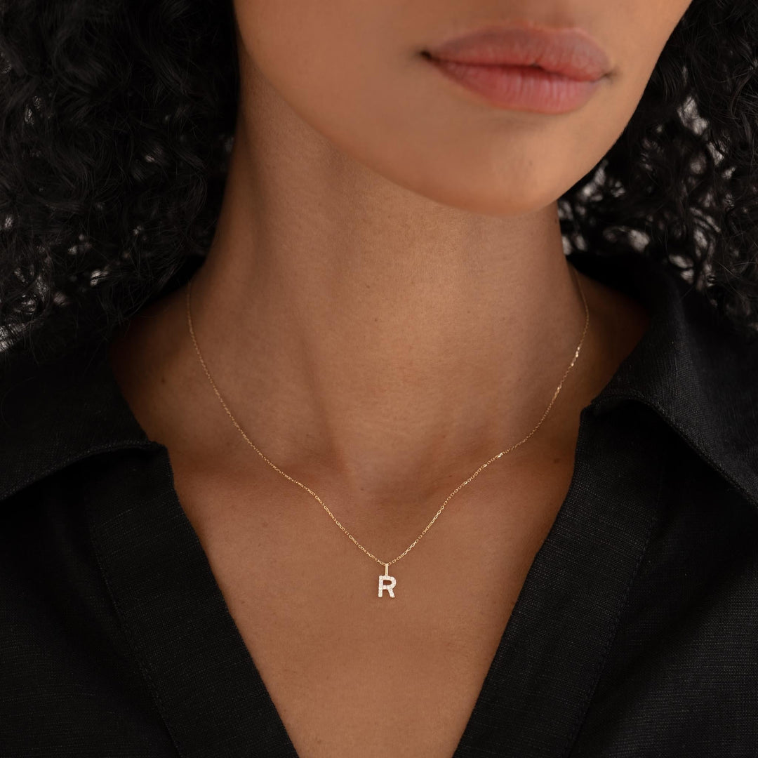 Close-up of a woman wearing the Diamond Initial Pendant 14k Gold - R on a delicate gold chain with a black shirt