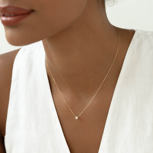 Close-up of woman wearing Bezel Set Diamond Necklace 14k Gold - Thais with a white linen sleeveless top