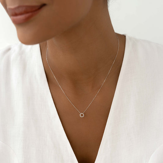 Close-up of a woman wearing the Diamond Sun Necklace White Gold - Lova on a white linen top against a neutral background