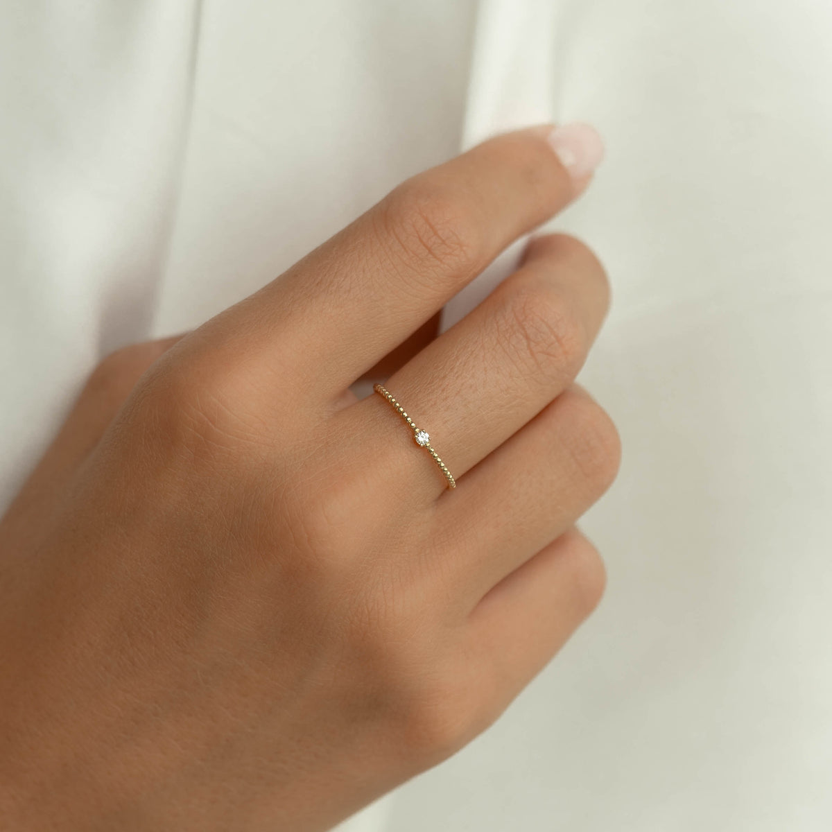 Close-up of hand wearing the Diamond Beaded Ring 14k Gold - Natalie with a single round diamond on a beaded band