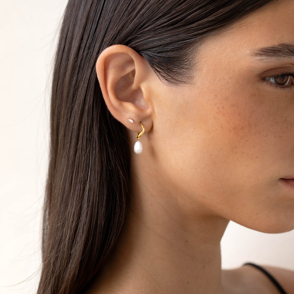 Close-up of a woman wearing Marquise Diamond Stud Earrings 14k Gold - Ardelle with smooth skin and dark hair against a neutral background