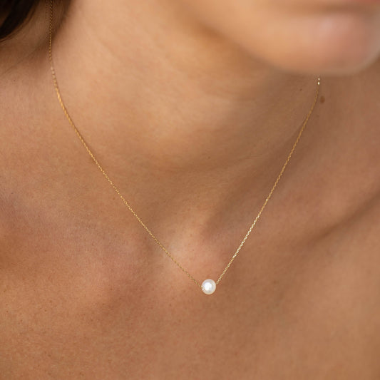 Close-up of a woman wearing the Floating Pearl Necklace - Caris with a single pearl on a delicate 14k gold chain