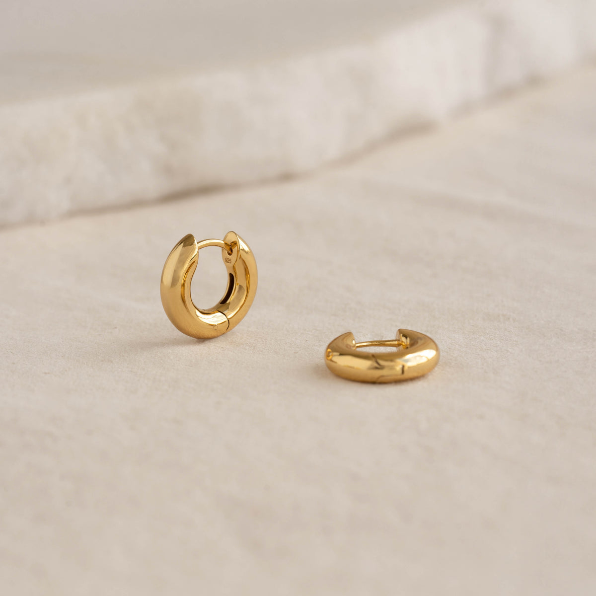 Chunky Huggie Hoop Earrings - Tove displayed on a light fabric surface with a soft neutral background