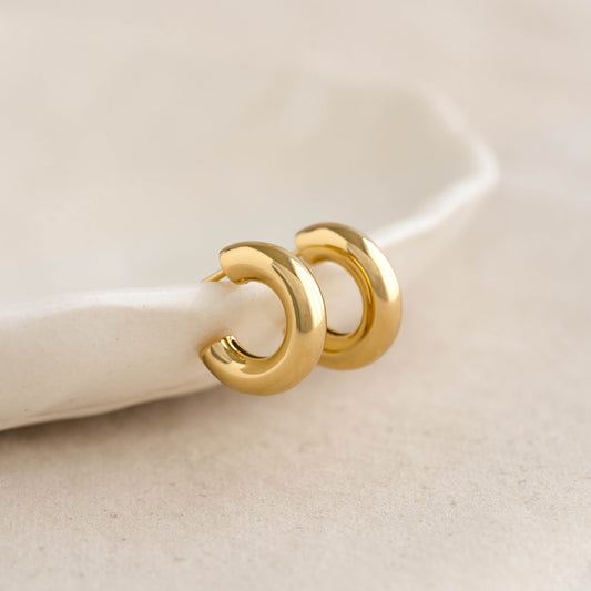 Close-up of Chunky Huggie Hoop Earrings - Giulia in gold vermeil resting on a beige fabric surface