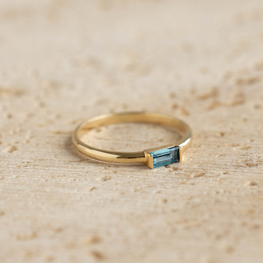 Close-up of Baguette Ring London Blue Topaz 14k Gold - Synne with rectangular blue gemstone on wooden surface
