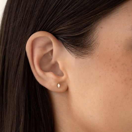 Close-up of a woman wearing Marquise Diamond Stud Earrings 14k Gold - Ardelle on her earlobe against a neutral background