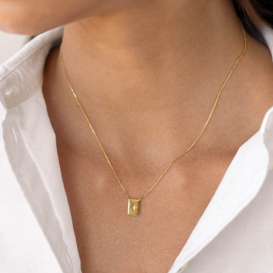 Close-up of a Diamond Star Necklace - Polaris with gold tag pendant featuring star engraving and diamond on a model wearing white shirt
