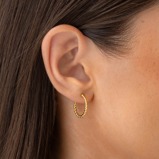 Close-up of a woman's ear wearing Braided Hoop Earrings - Hera in gold vermeil against a neutral background