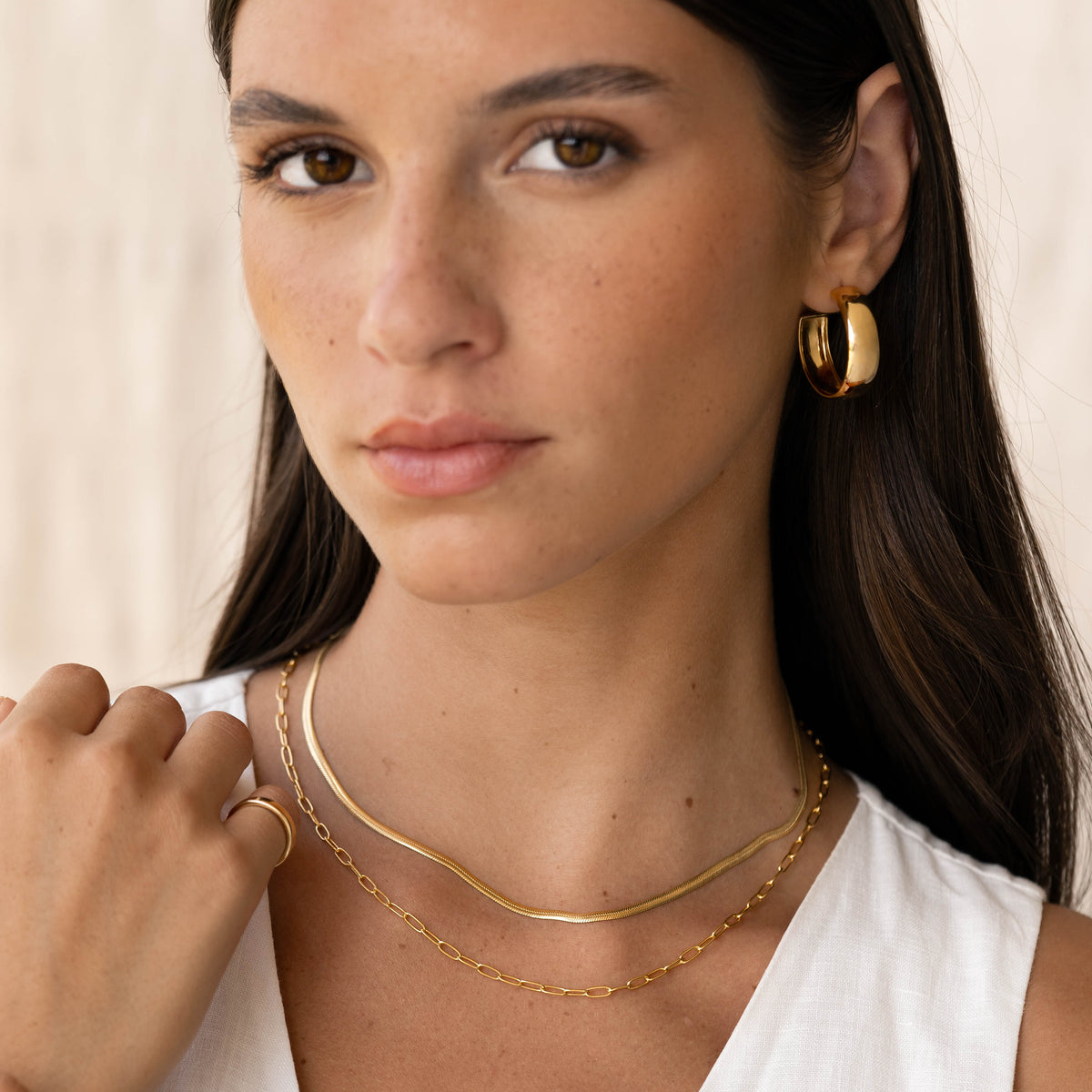 Close-up of woman wearing Chain Link Necklace 14k Gold with layered gold chains and gold hoop earrings on neutral background