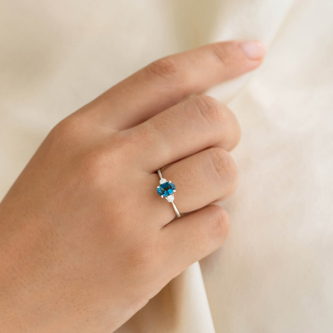 Close-up of a hand wearing the London Blue Topaz and Diamond Ring White Gold - Kindra on a neutral fabric background