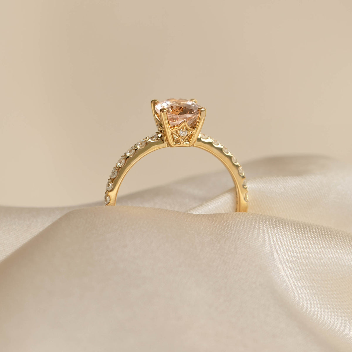 Close-up of Oval Morganite and Diamond Ring 14k Gold - Minette resting on soft beige satin fabric background