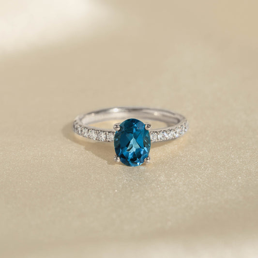 Oval London Blue Topaz and Diamond Ring White Gold - Minette with pavé diamonds and deep blue topaz on beige background