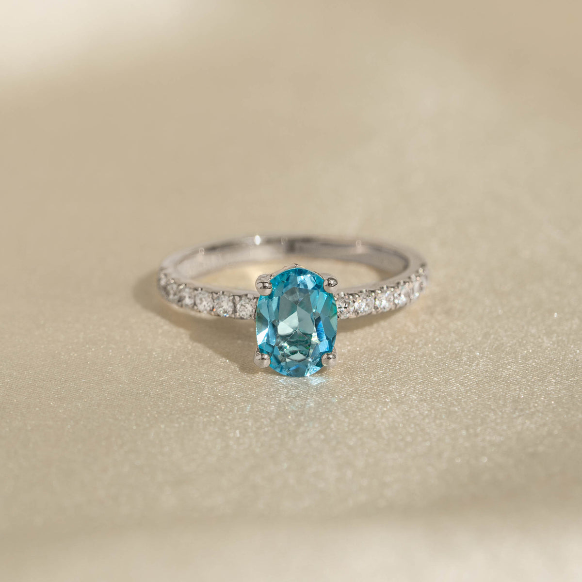 Oval Swiss Blue Topaz and Diamond Ring White Gold - Minette with a sparkling oval blue topaz and diamond pavé band on beige background