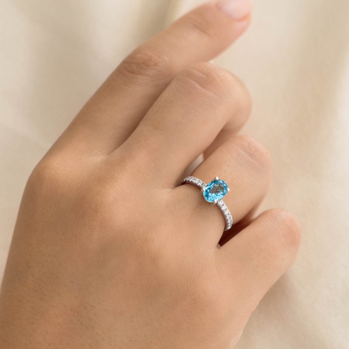 Oval Swiss Blue Topaz and Diamond Ring White Gold - Minette worn on a hand with a soft beige background