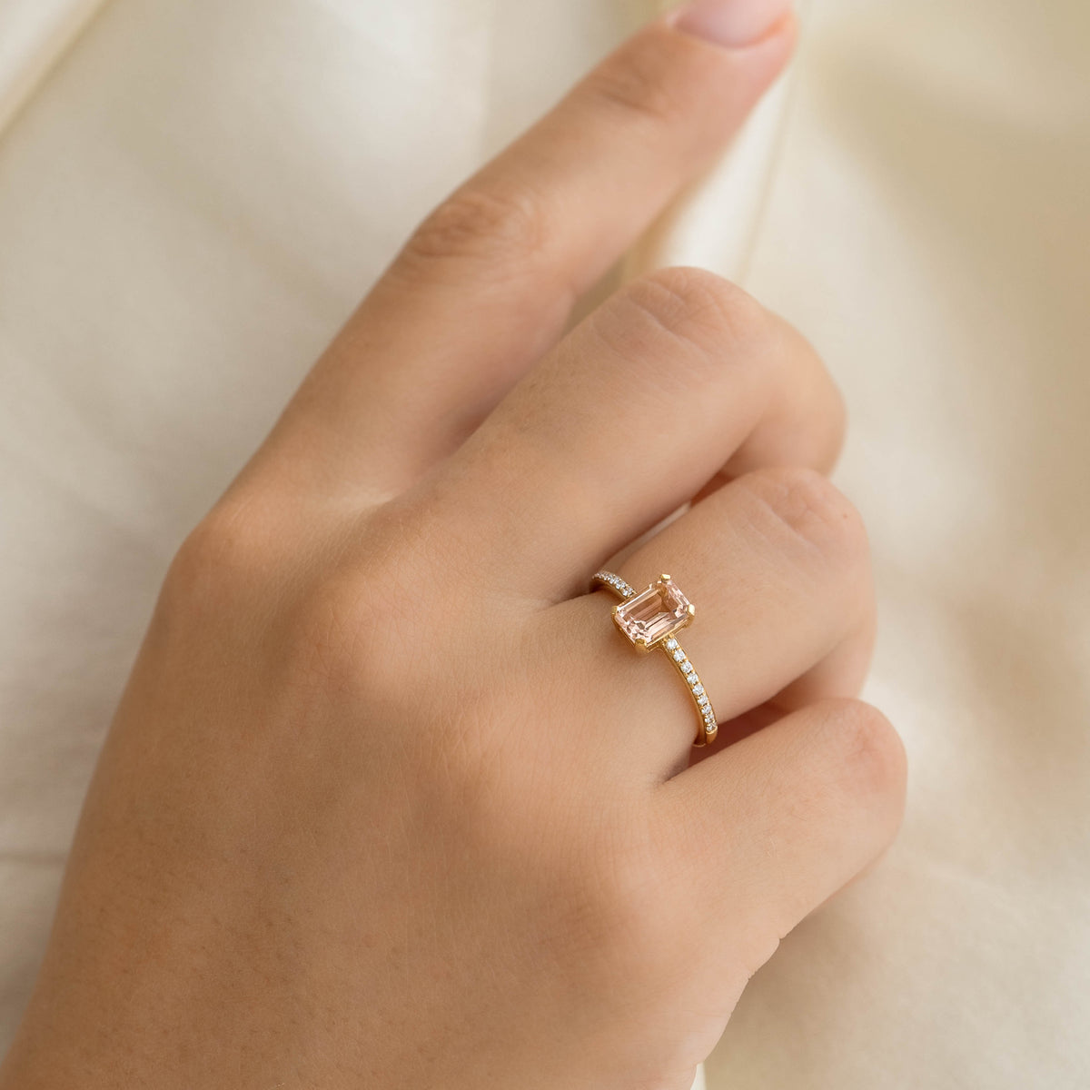 Close-up of a hand wearing the Baguette Morganite and Diamond Ring 14k Gold - Safiya with sparkling pavé diamonds on a neutral background