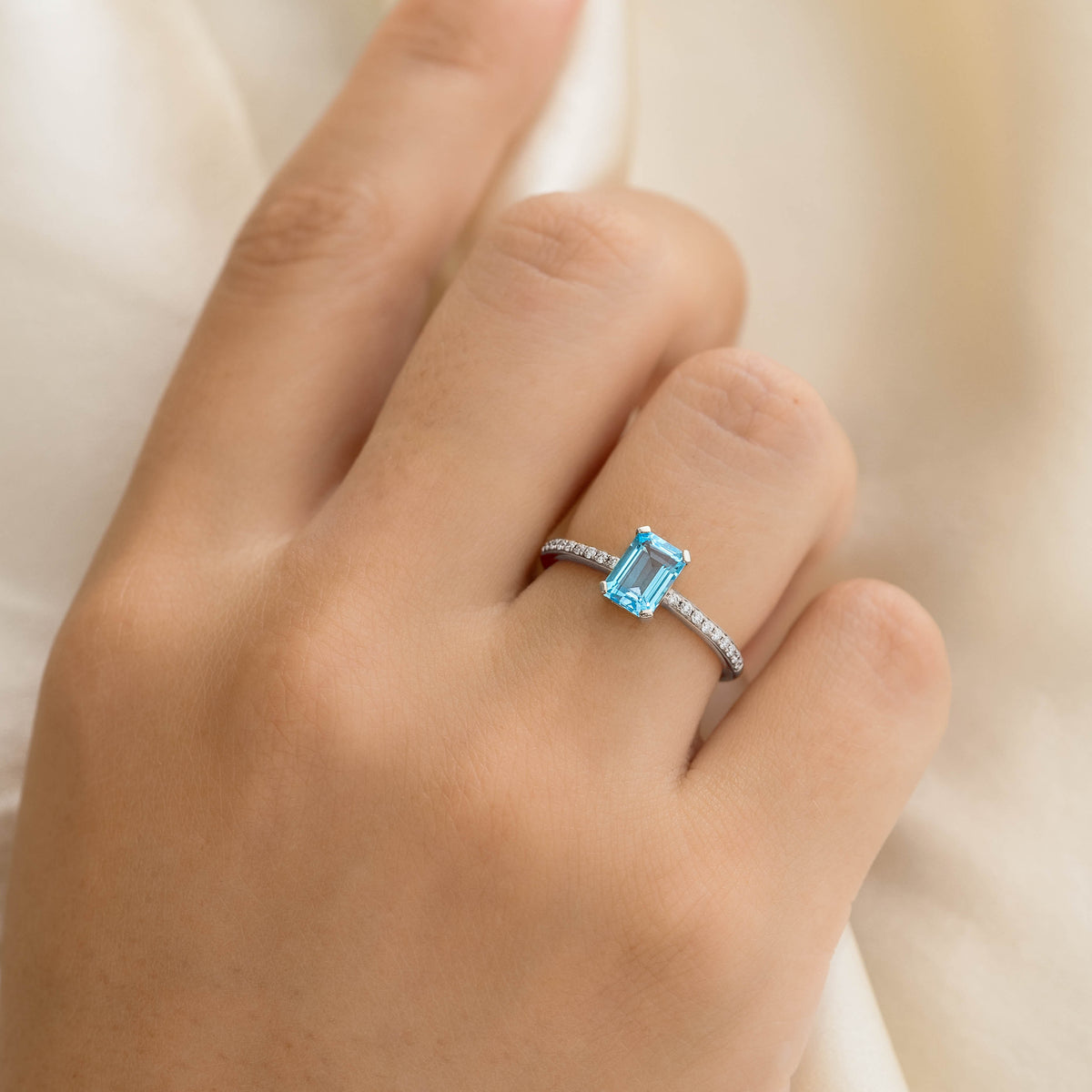 Close-up of a hand wearing Baguette Swiss Blue Topaz and Diamond Ring White Gold - Safiya on a cream fabric background