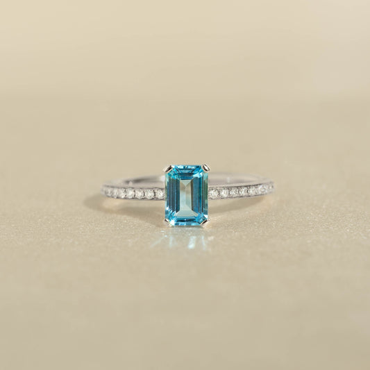 Close-up of Baguette Swiss Blue Topaz and Diamond Ring White Gold - Safiya featuring a blue topaz and pavé diamonds on a beige surface