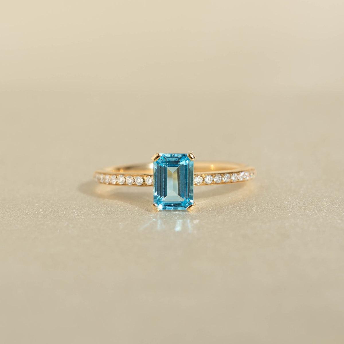 Baguette Swiss Blue Topaz and Diamond Ring 14k Gold - Safiya with a rectangular blue topaz and pavé diamond band on beige background