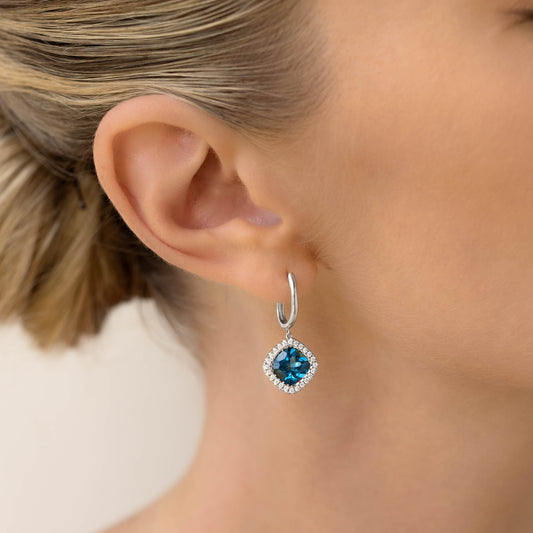 Close-up of ear wearing London Blue Topaz and Diamond Halo Drop Earrings White Gold - Elvira with soft neutral background