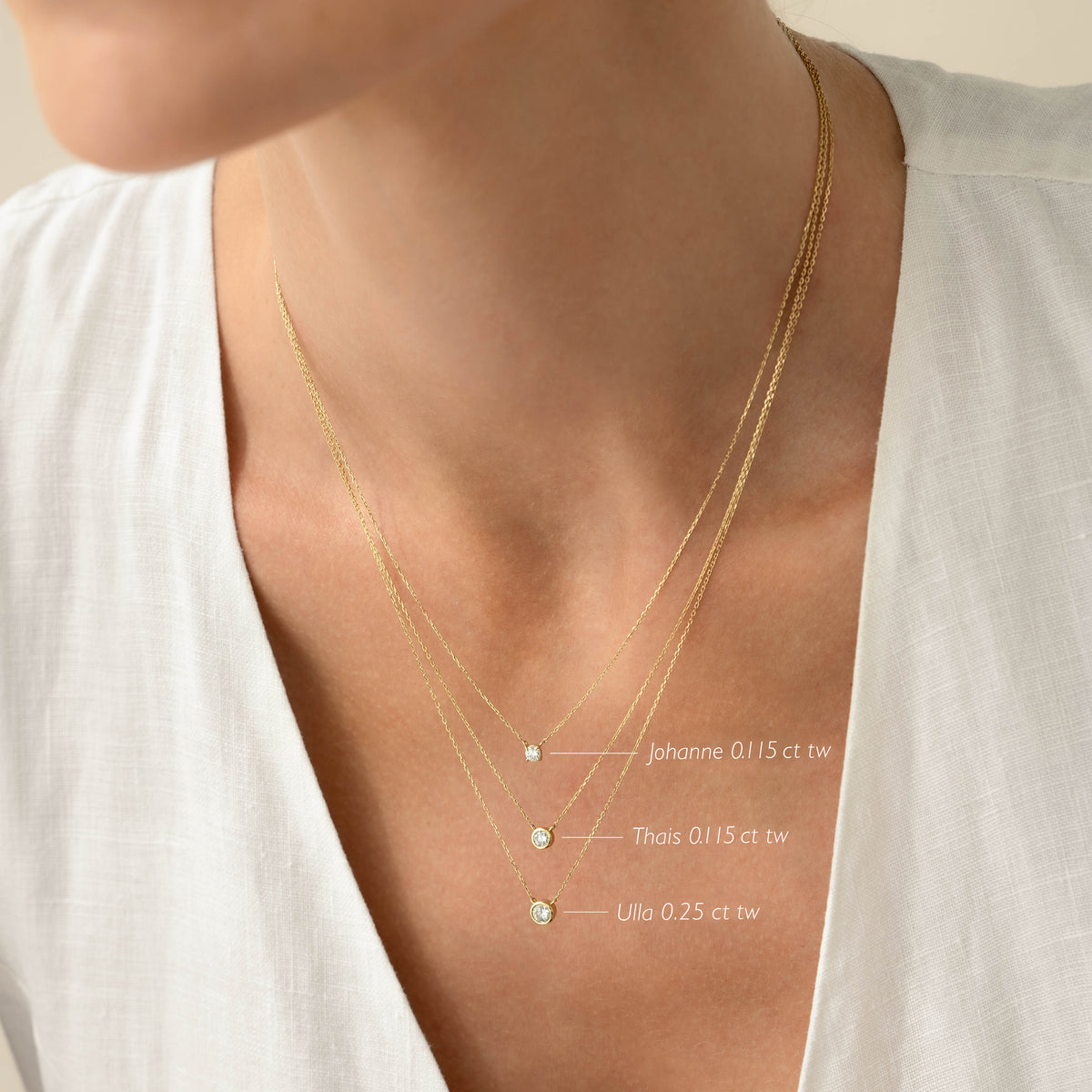 Close-up of a woman wearing layered necklaces featuring the Bezel Set Diamond Necklace 4mm 14k Gold - Ulla on a white top