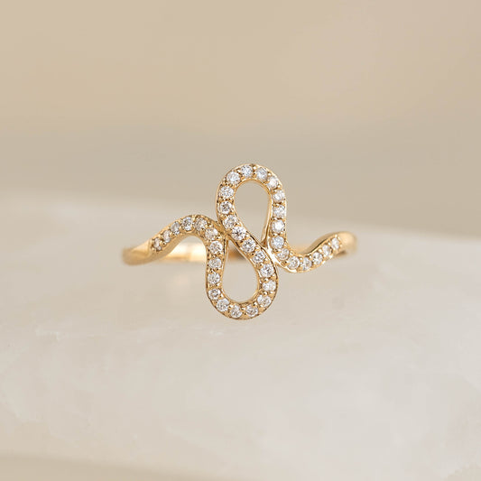 Close-up of Diamond Squiggle Ring 14k Gold with wavy band and pavé set brilliant diamonds on neutral background